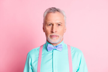 Photo portrait of serious confident elder man wearing teal shirt bowtie and suspenders isolated on pink color background