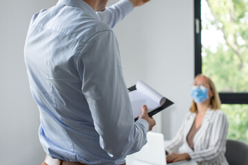 Work in a corporation during a pandemic. The man is giving a presentation and the woman wearing the face mask. Two business colleagues wearing protective face mask on a meeting during coronavirus.