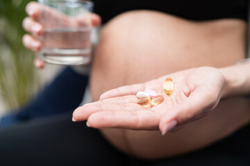 Healthcare, treatment, supplements. Young pregnant woman holding pills and glass of water in her hand before taking medication. Belly of pregnant woman and vitamin pills in the hand.