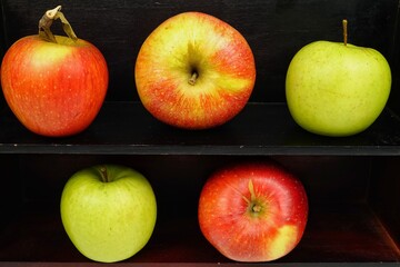 Red and green ripe apples lie on wooden shelves, background