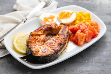 fried salmon with boiled egg and vegetables on white dish