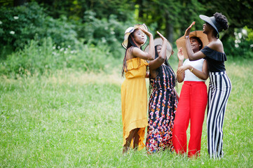 Group of four gorgeous african american womans wear summer hat spending time at green grass in park.
