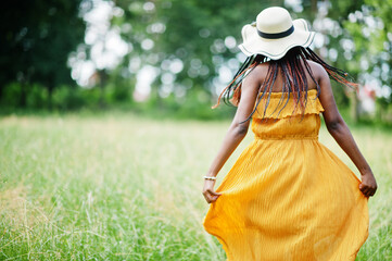Portrait of gorgeous african american woman 20s in wear in yellow dress and summer hat posing at...