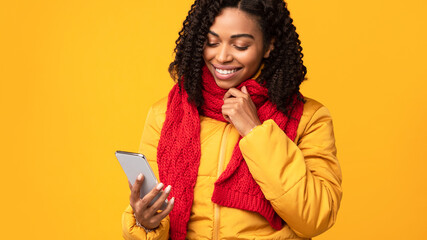Black Woman With Mobile Phone Reading Messages Over Yellow Background