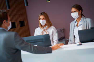 Businessman in mask at the reception of a hotel checking in