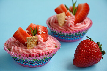 Beautiful cakes with strawberry pieces and pink cream on a blue background