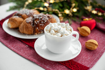 Christmas breakfast. Christmas morning. A cup of coffee or cocoa with marshmallows and sweets. On a red tablecloth next to a branch decorated with Christmas spruce. Selective focus.