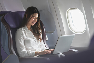 Asian young woman using laptop sitting near windows at first class on airplane during flight,Traveling and Business concept