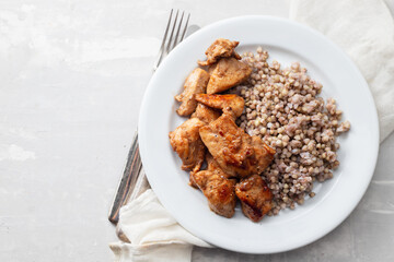boiled buchwheat with chicken in sauce on white plate on ceramic background