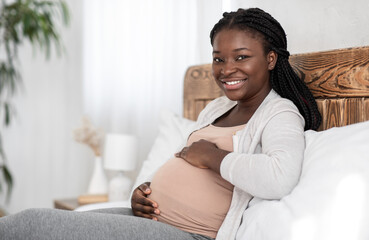 Enjoying Pregnancy. Cheerful Black Pregnant Woman Resting In Bed, Touching Her Belly