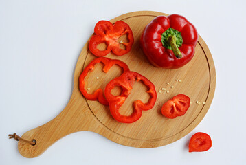 Rings of red bell pepper lie on a cutting board on a white background