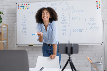 Fun English lesson and video streaming. Laughing african american lady stands near whiteboard with...