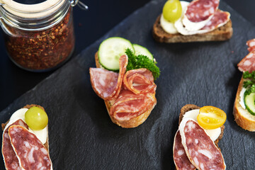 Sandwiches with smoked sausage on a black background. Meat delicacies decorated with greens and vegetables