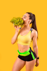 fitness girl in yellow and black sportswear eating lettuce. healthy food and slim figure. isolated on yellow background