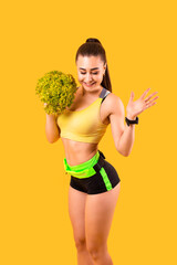 fitness girl with slim figure in yellow and black sportswear with lettuce. isolated on yellow background. looking down