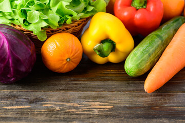 Colorful fresh vegetables on wooden table (cabbage, lettuce, bell pepper, cucumber, carrot and orange)