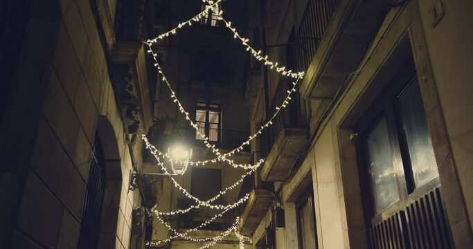 Smooth camera shot along narrow street at the night in the center of Barcelona in christmas holidays. View of old streets of Gotico quarter with christmas lights decorations
