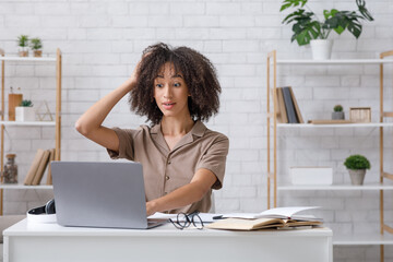 Difficult task or problems at online work. Surprised african american woman scratches her head and...