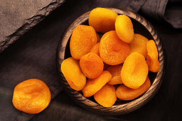 Dried apricots in a wooden plate on a dark background. Dry fruits on the kitchen table in retro style. View from above