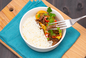 Roast beef with sweet pepper and white rice. White plate, garlic in the background, dark background.