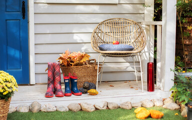 Cozy Autumn terrace with chair, plaid, rubber boots, baskets with chrysanthemums and pumpkins. Decorations in autumn patio for relax. Stylish fall decor on front porch home. Autumn wooden porch home	