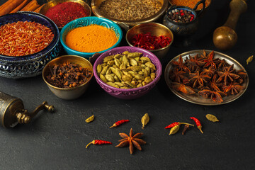 Bright spices and seasonings in colored bowls with ornaments, and a pepper mill on a black background, close-up with space