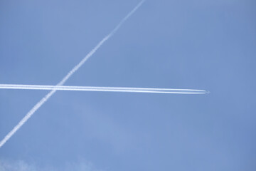 Long white plane traces in the clear cloudless blue sky and big passenger supersonic airplane with four jet engines flying high