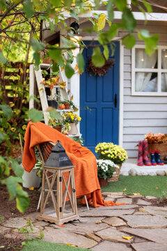 Cozy Autumn Patio With Chair, Plaid, Wooden Lantern, Potted Chrysanthemums And Pumpkins. Halloween. Decorations In Backyard For Relax In Autumn Garden. Stylish Fall Decor On Front Porch Home For Relax