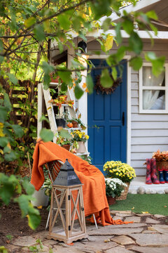 Cozy Autumn Patio With Chair, Plaid, Plants, Wooden Lantern, Potted Chrysanthemums. Halloween. Decorations In Backyard For Relax In Autumn Garden. Stylish Fall Decor On Front Porch Home. Thanksgiving 