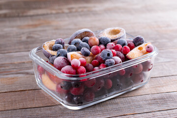 Containers of frozen mixed berries in snow - red currant, cranberry, raspberry, plum, bilberry, blueberry, black currant, strawberry