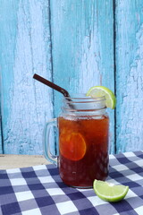 a glass jar of red lemon tea with honey is put on the towel table and wooden table with background of blue old wooden wall in the cafe