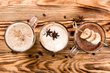 Hot chocolate with cinnamon sticks, anise, nuts and cocoa powder on rustic wooden background, top view