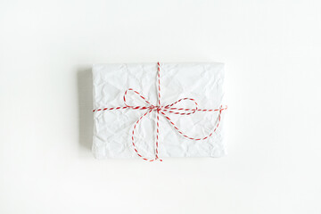Christmas, New year, anniversary composition. Gift wrapped in white paper with red and white rope on white table. Minimal concept. Flat lay, top view.