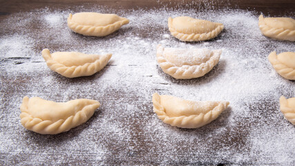Homemade dumplings, vareniki on an old wooden table, sprinkled with flour, space for text