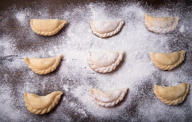 Homemade dumplings, vareniki on an old wooden table, sprinkled with flour, space for text