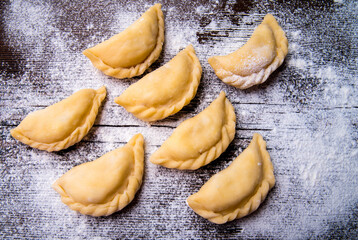 Homemade dumplings, vareniki on an old wooden table, sprinkled with flour, space for text