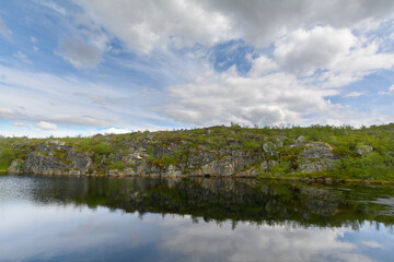 The reservoir is surrounded by hills and forest.Clouds are reflected in the water.Summer landscape.