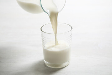 Pouring milk into glass on white table