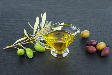 Delicious olive oil, black and green olives with leaves over black stone background