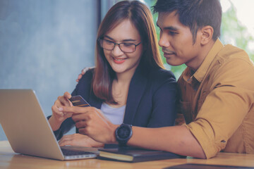 Asian young couple shopping online while sitting at workplace with credit card and laptop computer. Selected focus