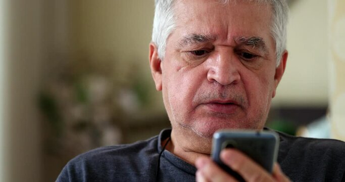 Frustrated senior using cellphone device at home. Upset older person looking at smartphone