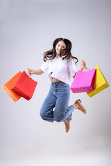 A beautiful Asian woman holding shopping bags of various colors and jumping with a happy expression on a white background. Holiday Shopping.