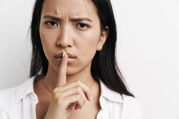 Beautiful displeased asian woman showing silence gesture at camera
