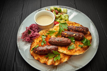 Beef josper kebab, with pine nuts, pita, sauce and vegetables, on a black background with copyspace