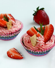 Pink cupcakes with cream and strawberry slices on a white background