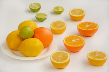 The layout of whole and sliced oranges, lemons, lime on a white plate