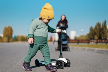 kid in green suit, yellow hat, baby with scooter in Park, active outdoor games