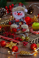 Fototapeta na wymiar Close-up toy snowman sits among burning garlands on wooden table