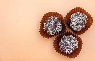 Coconut petit four is a juicy chocolate sponge cake with coconut filling and topping with coconut flakes. Mini cake on a beige background. Selective focus. Place for text.