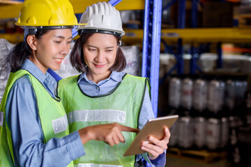 Warehouse woman wearing a hardhat standing cargo at goods or merchandise warehouse and check for control loading from Cargo freight ship for import and export by report on tablet. Teamwork concept